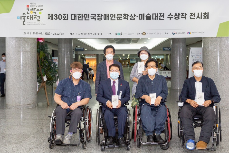 제30회 대한민국장애인문학상·미술대전 수상작전시회 플랜카드 아래 안내책자를 들고 찍은 장애인들 사진